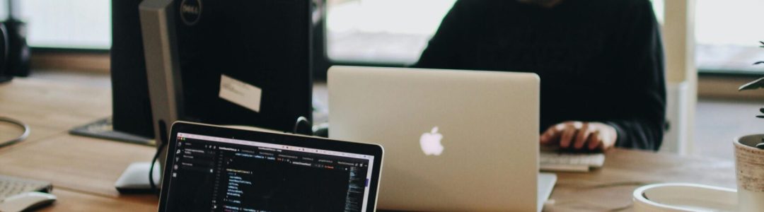 A web developer working on code in a modern office setting with multiple devices.